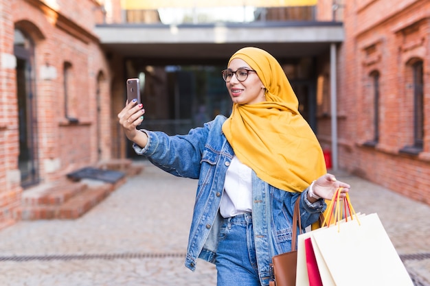 Koncepcja sprzedaży, technologii i zakupu - szczęśliwa arabska muzułmańska kobieta po selfie na zewnątrz