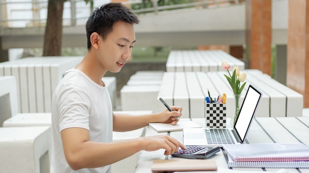 Koncepcja studiów online student w białej koszulce studiuje online za pomocą swojego nowego białego laptopa i kalkulatora w klasie rachunkowości.