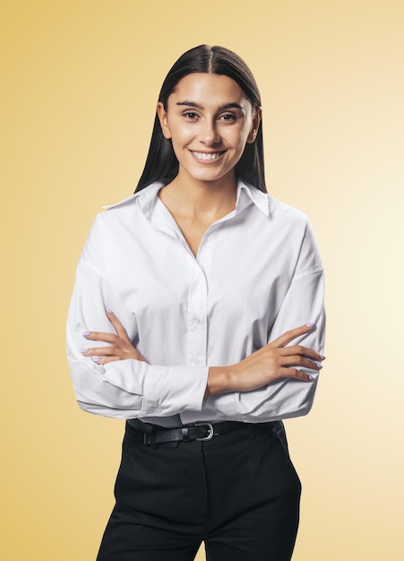 Koncepcja sukcesu biznesowego z młodą uśmiechniętą kobietą składającą ręce w białej koszuli i czarnych spodniach na abstrakcyjnym jasnopomarańczowym tle z bliska na białym tle