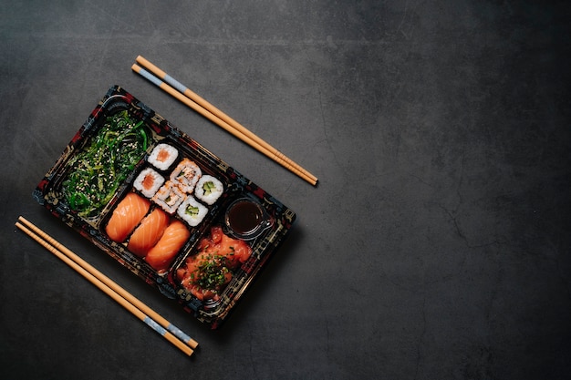 Koncepcja sushi na wynos. Pudełko z sushi. Z roladkami sushi i pałeczkami. Maki. Sashimi. Łosoś. Tuńczyk. Wasabi. Azjatyckie. Język japoński.