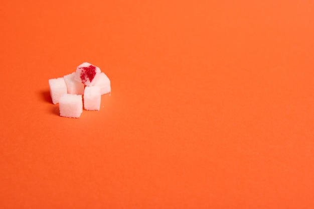 Koncepcja świadomości Światowego Dnia Cukrzycy, 14 listopada. Czysty rafinowany biały cukier w kostkach z kroplą krwi, odizolowany na kolorowym pomarańczowym tle z miejscem na kopię na reklamę medyczną