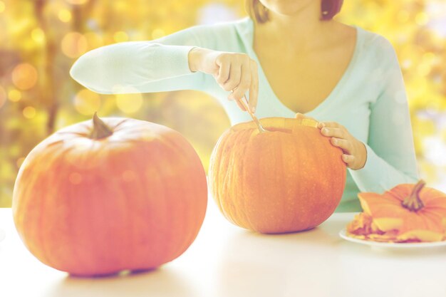 koncepcja świąt, dekoracji, rzemiosła i ludzi - zbliżenie kobiety rzeźbiącej dynie na halloween