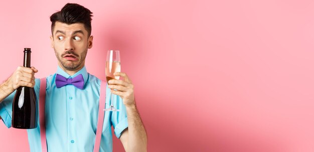 Zdjęcie koncepcja świąt i uroczystości zdezorientowany pijany facet patrząc na pustą butelkę szampana trzymając gla