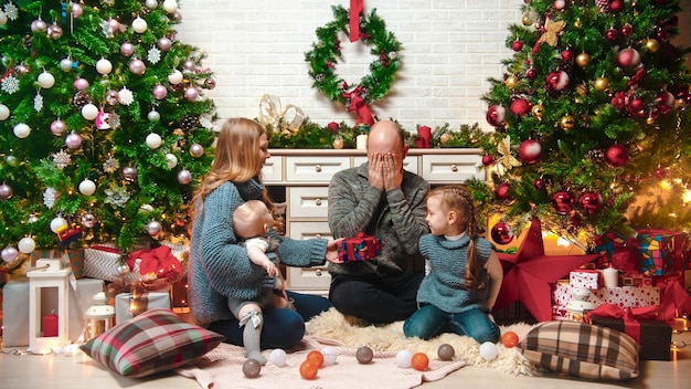 Koncepcja świąteczna szczęśliwa udana rodzina siedzi w świątecznym otoczeniu i wymienia prezenty tata siedzący z zamkniętymi oczami