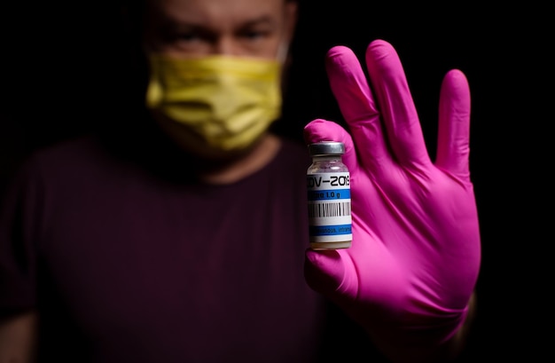 Koncepcja szczepień Szczepionka w męskich rękach Ciemne tło Mężczyzna trzyma lek na covid