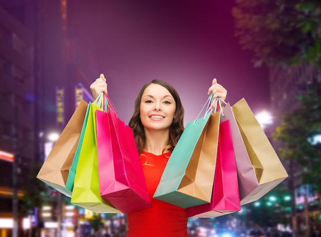 koncepcja szczęścia, konsumpcjonizmu, sprzedaży i ludzi - uśmiechnięta młoda kobieta z torbami na zakupy na nocnym tle miasta