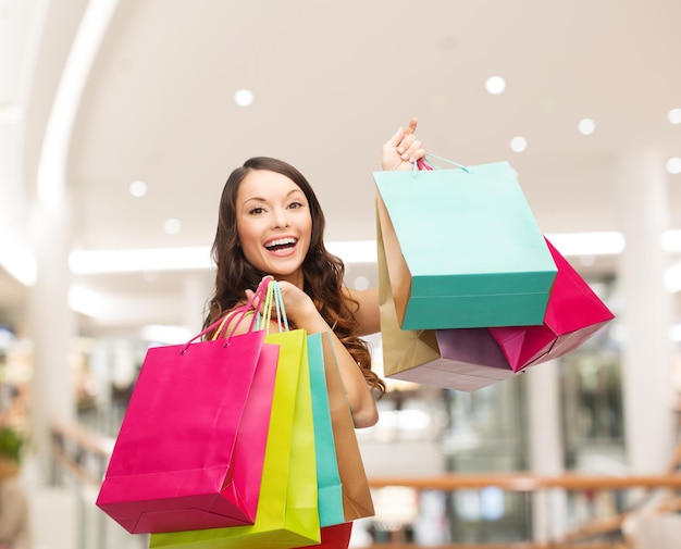 koncepcja szczęścia, konsumpcjonizmu, sprzedaży i ludzi - uśmiechnięta młoda kobieta z torbami na zakupy na tle centrum handlowego