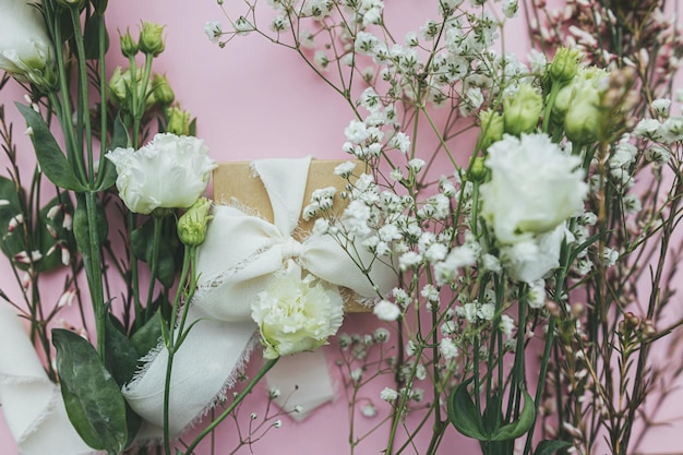 Koncepcja szczęśliwego dnia kobiet i dnia matki Stylowy prosty prezent ze wstążką i pięknymi delikatnymi kwiatami na różowym tle leżał płasko Kwiatowa kartka z życzeniami lub baner