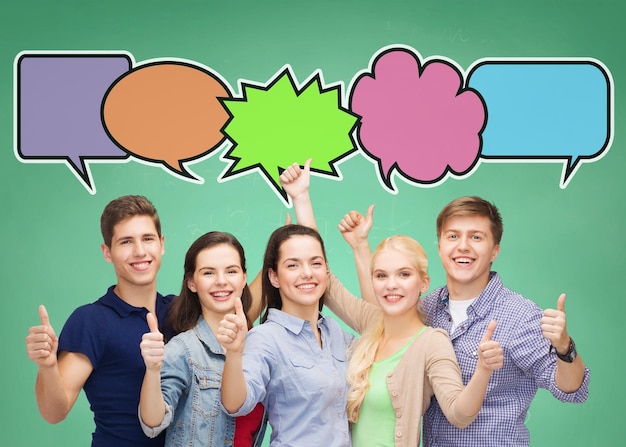 Zdjęcie koncepcja szkoły, edukacji, komunikacji, gestów i ludzi - grupa uśmiechniętych nastolatków pokazujących kciuki w górę na zielonym tle tablicy z bąbelkami tekstowymi