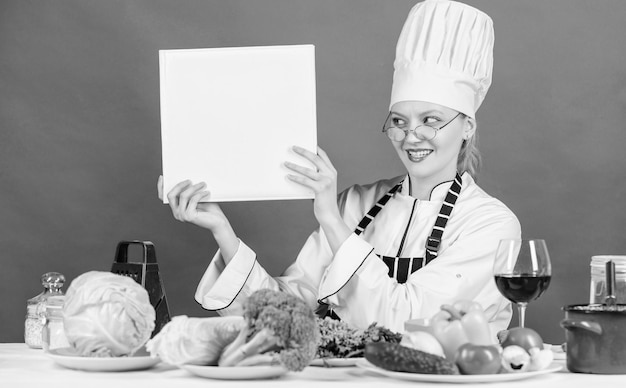 Koncepcja szkoły kulinarnej Kobieta w kapeluszu i fartuchu wie wszystko o sztuce kulinarnej Tradycyjna kuchnia Ekspert kulinarny Kobieta kucharz gotuje zdrowe jedzenie Dziewczyna czyta książkę Najlepsze przepisy kulinarne