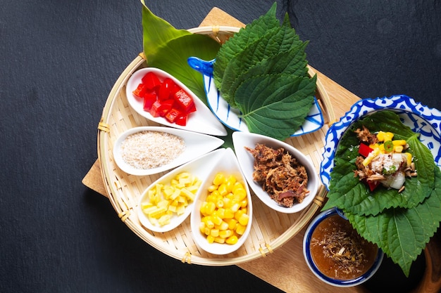 Zdjęcie koncepcja tajskiego jedzenia fusion tajska przekąska ziołowa i tuńczykowa miang kham okład z jednym kęsem przez perilla leaveshiso z mieszanką ziół sos z cukru kokosowego na czarnym tle z miejscem na kopię