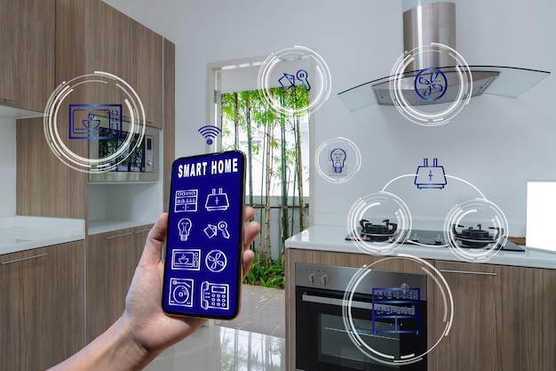 Koncepcja technologii inteligentnego domu i rzeczywistości rozszerzonej, dłoń trzymająca smartfona przedstawiająca ekran sterowania inteligentnego domu i ikonę nad luksusową kuchnią