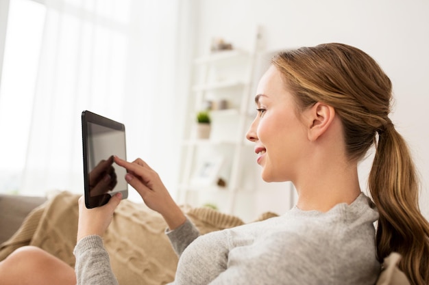 koncepcja technologii, internetu i ludzi - uśmiechnięta kobieta siedzi na kanapie z komputerem typu tablet pc w domu