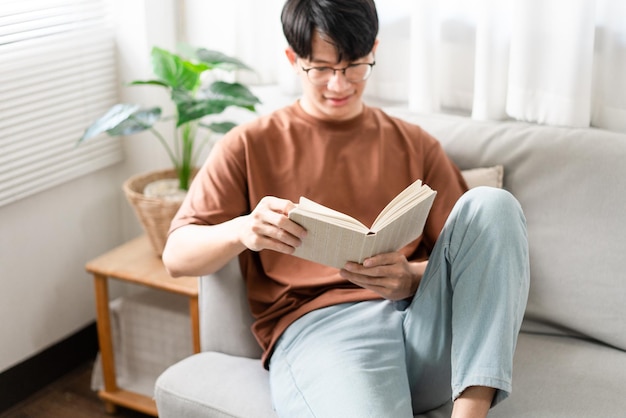 Koncepcja technologii Mężczyzna w okularach siedzi na szarej sofie i czyta książkę