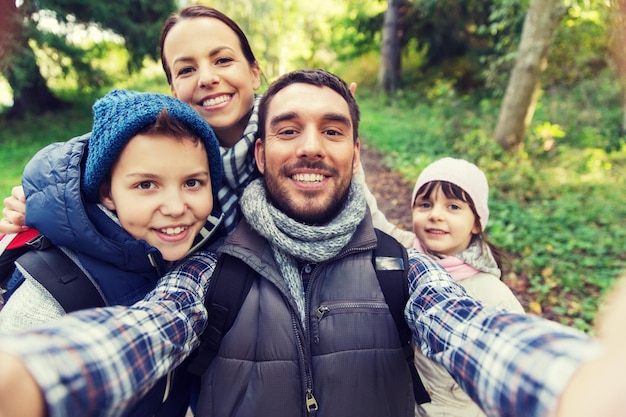 koncepcja technologii, podróży, turystyki, wędrówek i ludzi - szczęśliwa rodzina z plecakami biorącymi selfie i piesze wycieczki