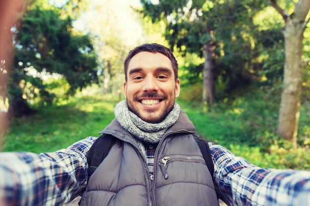 koncepcja technologii, podróży, turystyki, wędrówek i ludzi - szczęśliwy człowiek z plecakiem biorący selfie i piesze wycieczki