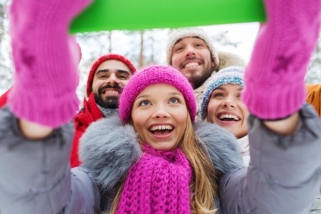 koncepcja technologii, pory roku, przyjaźni i ludzi - grupa uśmiechniętych mężczyzn i kobiet biorących komputer typu tablet PC selfie w zimowym lesie
