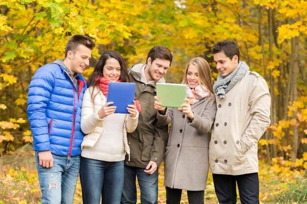 koncepcja technologii, pory roku, przyjaźni i ludzi - grupa uśmiechniętych mężczyzn i kobiet z komputerami typu tablet PC w jesiennym parku