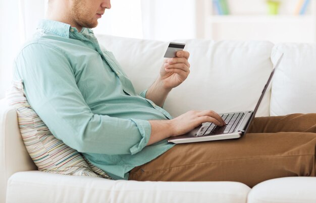 Zdjęcie koncepcja technologii, zakupów, bankowości, domu i stylu życia - zbliżenie mężczyzny z laptopem i kartą kredytową w domu