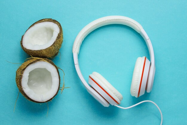 Koncepcja twórcza miłośnika muzyki. Lato w tle. białe klasyczne słuchawki, połówki kokosa na niebieskim tle. Widok z góry