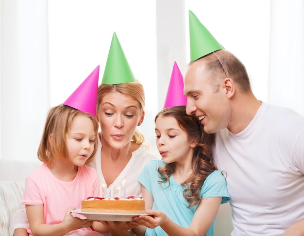 koncepcja uroczystości, rodziny, świąt i urodzin - szczęśliwa rodzina z dwójką dzieci w czapkach z ciastem w domu