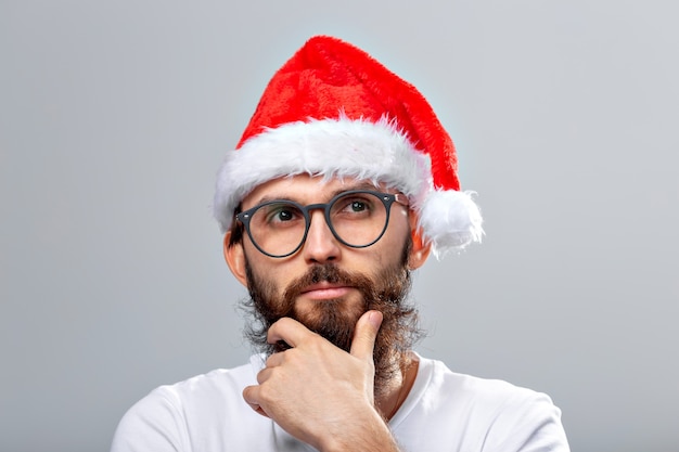 Koncepcja wakacje i ludzie - portret przystojny brutalny mężczyzna w kapeluszu Boże Narodzenie. Nad szarym
