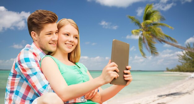 koncepcja wakacje, wakacje, podróże, technologia i miłość - uśmiechnięta para z komputerem typu tablet pc biorąca selfie na tle tropikalnej plaży