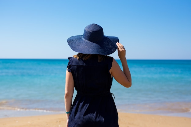 Koncepcja Wakacji I Podróży - Widok Z Tyłu Kobiety W Sukience I Kapeluszu Na Tle Plaży Latem