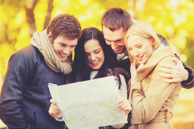 koncepcja wakacji i turystyki - grupa przyjaciół lub pary z mapą turystyczną w jesiennym parku