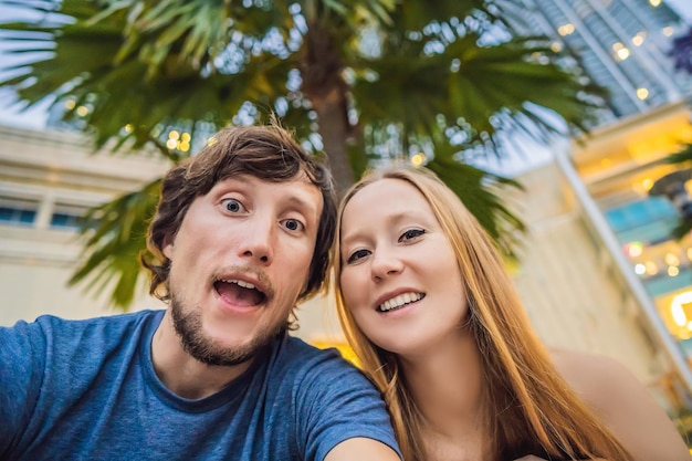 Koncepcja wakacji i wakacji w podróży Szczęśliwa para bawi się przy selfie nad parkiem z tłem palm i drapaczami chmur