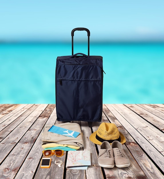 koncepcja wakacji letnich, turystyki i obiektów - torba podróżna, mapa, bilet lotniczy i ubrania z osobistymi rzeczami na drewnianej podłodze i tle morza