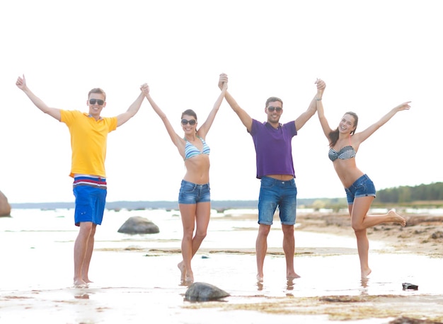 koncepcja wakacji, wakacji, turystyki, podróży i ludzi - grupa szczęśliwych przyjaciół trzymających się za ręce na plaży