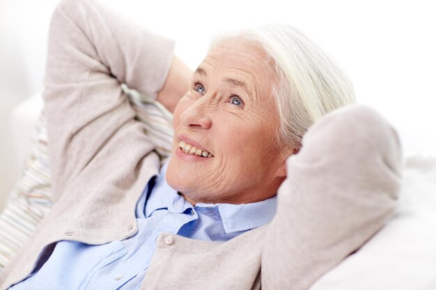 Zdjęcie koncepcja wieku, relaksu i ludzi - szczęśliwa uśmiechnięta starsza kobieta odpoczywa na kanapie i marzy w domu