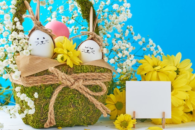 Koncepcja Wielkanoc. Jajka w koszu dekorującym z kwiatami na błękitnym tle