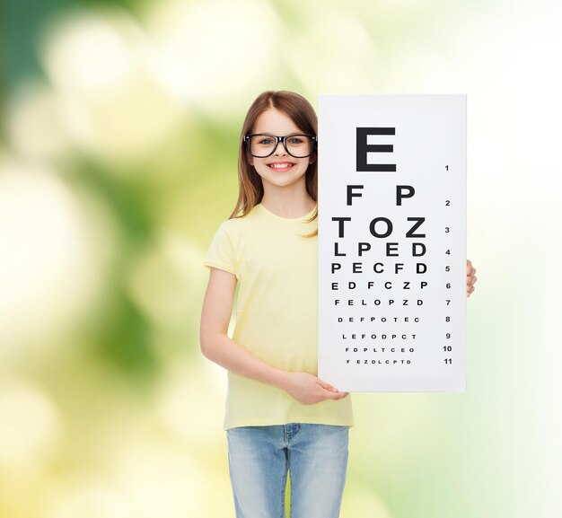 Zdjęcie koncepcja wizji, zdrowia i ludzi - uśmiechnięta dziewczynka w okularach z wykresem sprawdzania oczu