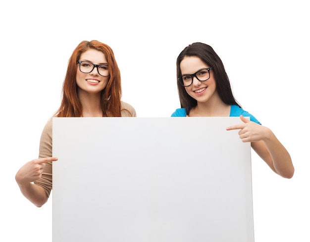 koncepcja wizji, zdrowia, reklamy i ludzi - dwie uśmiechnięte dziewczyny w okularach wskazujące palcami na białą pustą tablicę
