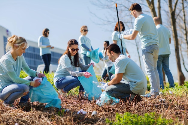 koncepcja wolontariatu, działalności charytatywnej, sprzątania, ludzi i ekologii - grupa szczęśliwych wolontariuszy z miejscem do czyszczenia worków na śmieci w parku
