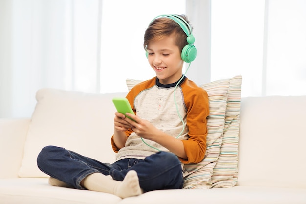 koncepcja wypoczynku, dzieci, technologii i ludzi - uśmiechnięty chłopiec ze smartfonem i słuchawkami słuchający muzyki lub grający w gry w domu