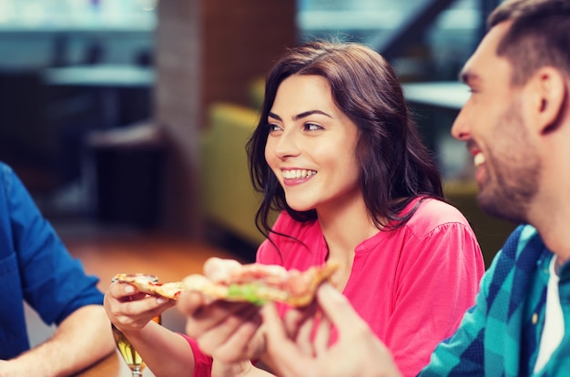 koncepcja wypoczynku, jedzenia i napojów, ludzi i wakacji - uśmiechnięci przyjaciele jedzący pizzę i pijący piwo w restauracji lub pubie