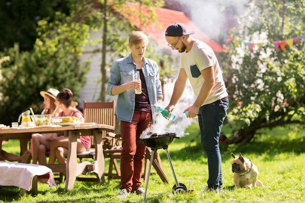 koncepcja wypoczynku, jedzenia, ludzi i wakacji - przyjaciele gotują mięso na grillu na letniej imprezie plenerowej