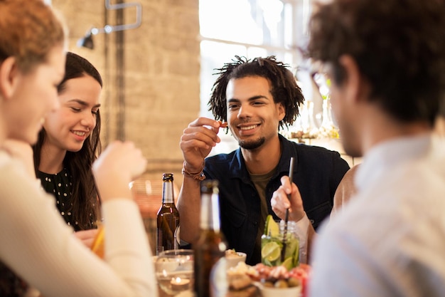koncepcja wypoczynku, jedzenia, napojów, ludzi i wakacji - szczęśliwi przyjaciele jedzą i piją w barze lub kawiarni