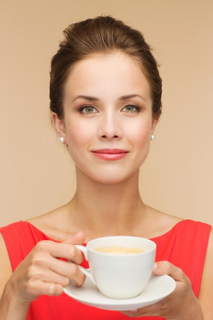 koncepcja wypoczynku, szczęścia i picia - uśmiechnięta kobieta w czerwonej sukience z filiżanką kawy
