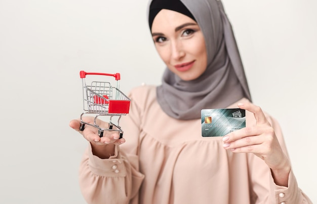 Koncepcja zakupów. Arabska kobieta z kartą kredytową i koszykiem