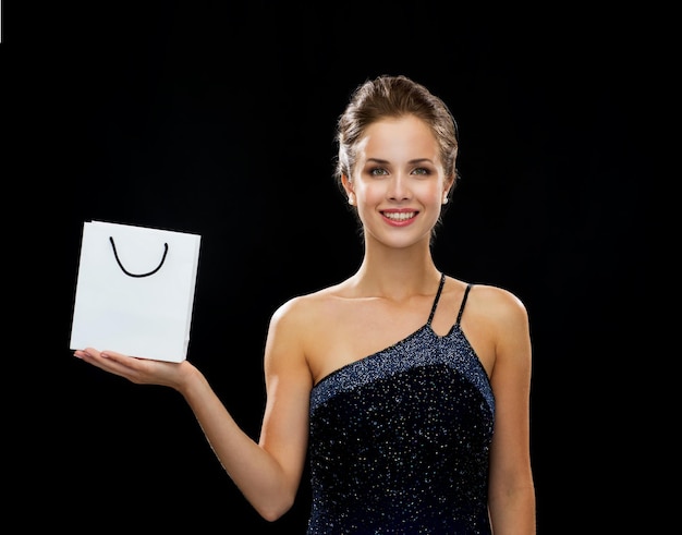 koncepcja zakupów, luksusu, reklamy, świąt i sprzedaży - uśmiechnięta kobieta z białą pustą torbą na zakupy na czarnym tle