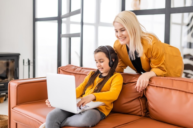 Koncepcja zakupów online lub płatności. Matka uczy córkę za pomocą laptopa w domu. Siedząc na kanapie.
