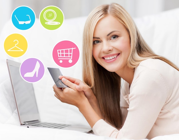 Zdjęcie koncepcja zakupów online, sprzedaży, mody i ludzi - szczęśliwa kobieta lub gospodyni domowa z laptopem i kartą kredytową w domu