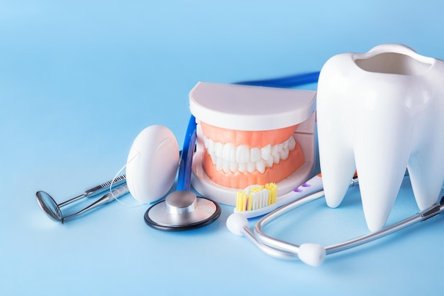 Koncepcja zdrowia i pielęgnacji zębów. Lusterko dentystyczne z sondą eksploratora, szczoteczką do zębów, nicią dentystyczną, modelem ludzkiej szczęki i białym zębem ze stetoskopem na niebieskim tle.