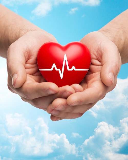 koncepcja zdrowia rodzinnego, dobroczynności i medycyny - zbliżenie rąk trzymających czerwone serce z kardiogramem na tle błękitnego nieba i chmur
