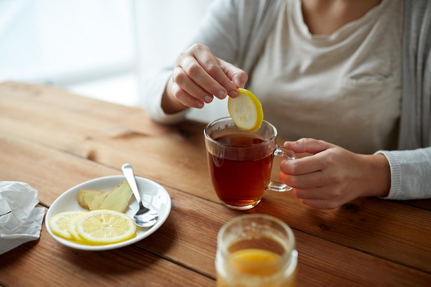 koncepcja zdrowia, tradycyjnej medycyny i etnonauki - zbliżenie kobiety dodającej cytrynę do filiżanki herbaty