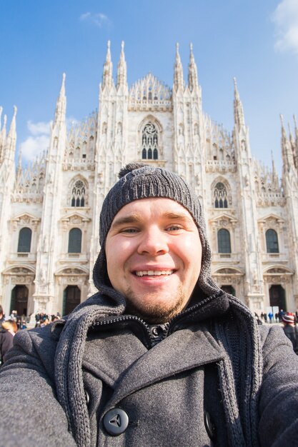 Koncepcja zimowych podróży, wakacji i wakacji - młody zabawny człowiek robi selfie w pobliżu katedry w Mediolanie Duomo di Milano, Włochy.